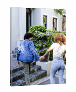 Young diverse couple holding hands walking outside, enjoying sunny day together