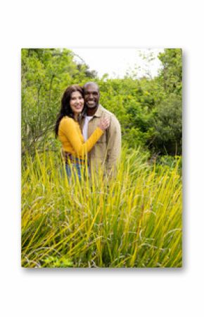 multiracial couple embracing in lush garden, appreciating nature together with smiles