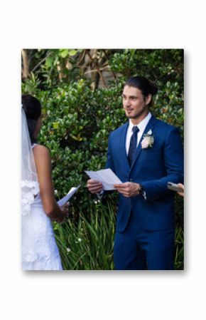 Groom reading vows to bride outdoors, surrounded by joyful wedding party