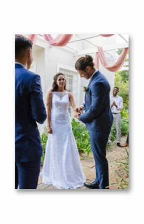 Bride and groom exchanging rings outdoors, surrounded by joyful friends