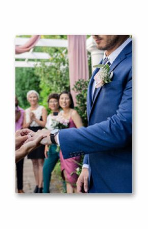 Exchanging rings during outdoor wedding ceremony, surrounded by joyful friends