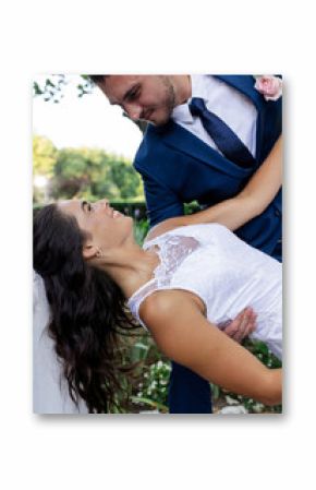 Groom in blue suit joyfully dipping bride in white dress outdoors