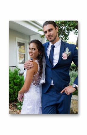 Bride and groom smiling outdoors, embracing in elegant wedding attire