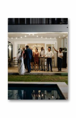 Bride and groom kissing by poolside, guests celebrating with joyful expressions, copy space