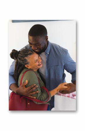 African American couple hugging joyfully at home, holding gift bag and smiling