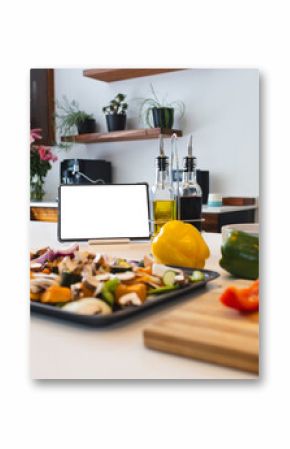 A tablet with a blank screen stands among various cooking ingredients on a kitchen counter