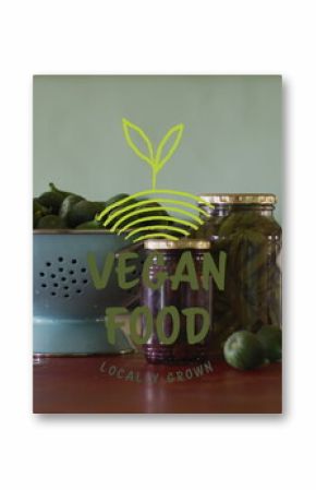 A bowl and jar labeled VEGAN FOOD sit on table surrounded by green fruits