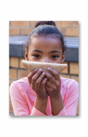 In school courtyard, african american girl holding sandwich and looking at camera