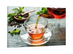 Pouring black tea into glass cup on wooden table
