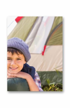 Middle Eastern boy leaning on rolled-up sleeping bag at grassy campsite beside beige green tent