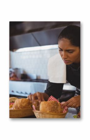 Indian woman chef adding rolls into baskets beside sandwiches on counter in kitchen, copy space