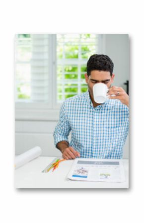 Middle Eastern man sitting at kitchen countertop drinking coffee from mug and reviewing layout