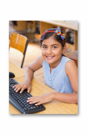 Indian child wearing rainbow bow headband typing on keyboard at computer lab desk with world map