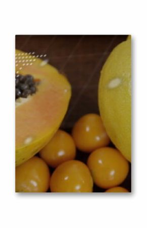 Displaying halved papaya revealing orange flesh and seeds on dark wood board, with kumquats, lemon