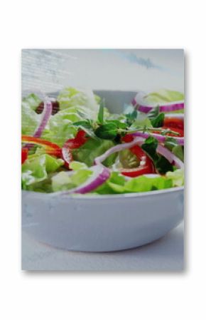 White bowl containing lettuce, red peppers, purple onion rings and green herb sprigs in studio