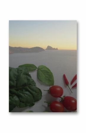 Displaying produce on white seaside terrace table, with kale, cherry tomatoes, basil and orange