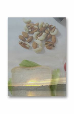 Displaying nuts, bread slices, fruits and vegetables on pale work surface, with lake sunset overlay
