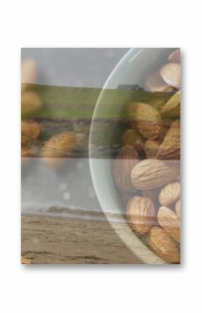Showing white ceramic bowl holding whole almonds on coastal beach under overcast sky, copy space