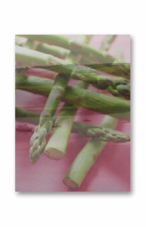 Displaying green asparagus spears resting on pink surface with sailboats, harbor water, hillside