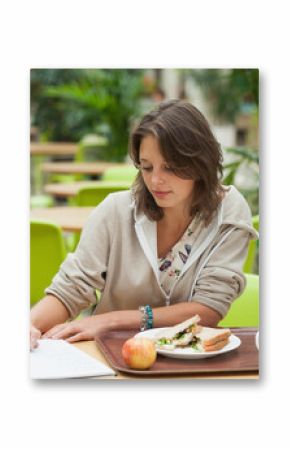 Spiral notebook lying open on round table in food court, with sandwich, apple, mug, water bottle