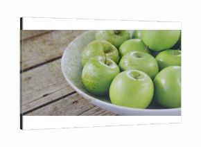 Displaying white ceramic bowl holding shiny green apples on wooden kitchen table, copy space