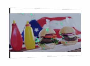 Two mini hamburgers resting on wooden board in studio, with flag backdrop ketchup mustard eco icons