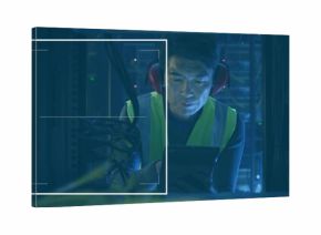 Kneeling Korean technician inspecting tablet in data center, with LEDs server racks safety vest