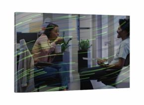 Two mid adult coworkers eating lunch in open-plan office area, with chopsticks and sandwich