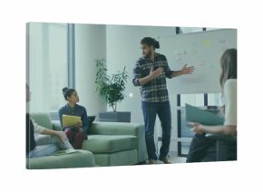 Standing presenter in plaid shirt and jeans gesturing at whiteboard in glass office, with notebooks