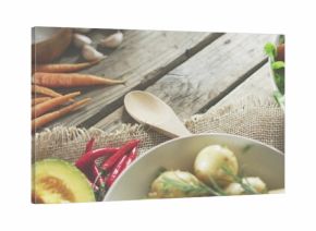 Displaying bowl of boiled potatoes with herbs on wooden table, with wooden spoon, carrots, avocado