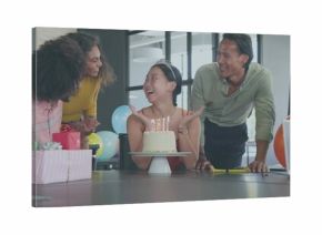Celebrating team gathering around seated woman with tiara and red dress in office with cake, laptop