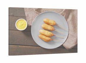 Presenting plate with four skewered corn dogs on dark tabletop, with mustard bowl and linen napkin