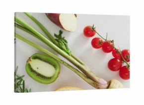 Composing produce flat-lay on white table, showing cherry tomatoes vine, halved kiwi, rosemary