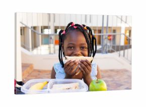 Happy african american schoolgirl having healthy lunch eating sandwich at elementary school