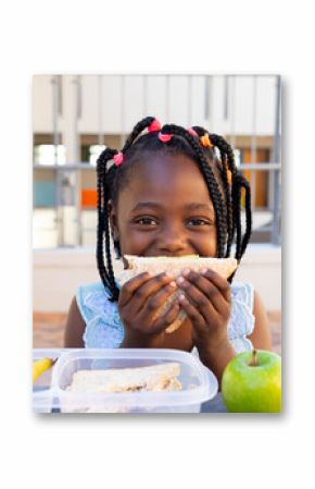 Happy african american schoolgirl having healthy lunch eating sandwich at elementary school