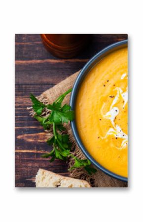 Pumpkin and carrot soup with cream and parsley on dark wooden background Top view Copy space