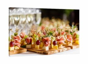 the buffet at the reception. Glasses of wine and champagne. Assortment of canapes on wooden board. Banquet service. catering food, snacks with cheese, jamon, prosciutto and fruit