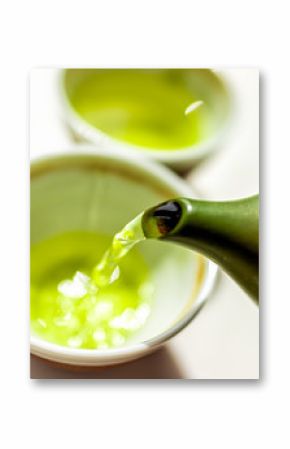 Closeup of green clay tea pot teapot on white table background and pouring liquid motion of colorful vibrant Japanese sencha or genmaicha drink during ceremony