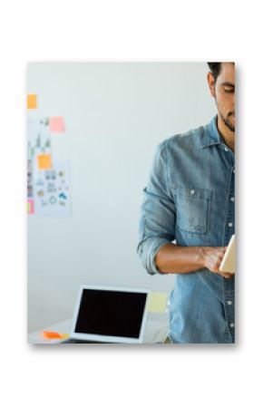 Middle Eastern pro standing reviewing tablet in modern office with sticky notes collage and laptop