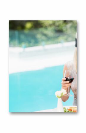 Glass of red wine resting on tabletop beside salad plate and white flower near turquoise pool
