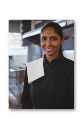 Indian female chef wearing black jacket smiling in kitchen by prep counter with plated sandwiches