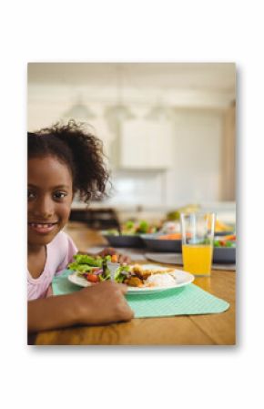 Child is eating salad, rice, chicken on mint green placemat at wood table in modern kitchen