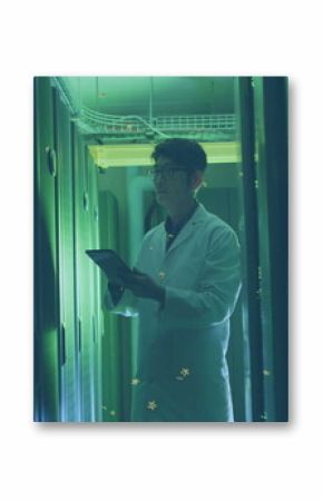 Korean technician in white lab coat inspecting server racks in data center, with tablet computer