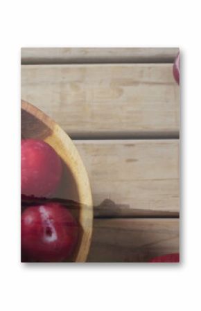 Displaying wooden bowl holding red plums on rustic tabletop, with scattered plums, copy space