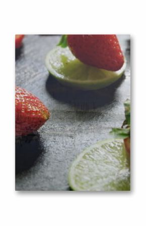 Displaying ripe red strawberry perched on lime slices on dark slate board, with sliced strawberries