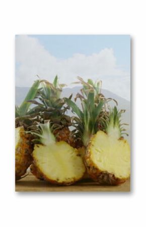 Displaying cluster of four pineapples arranged on wooden table outdoors, with mountain backdrop