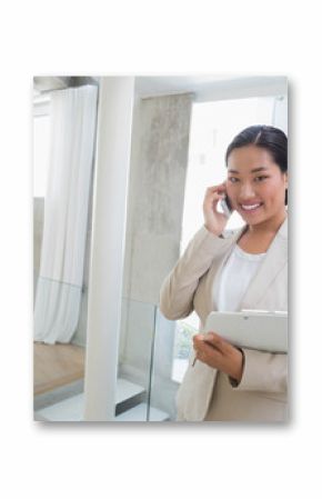 Korean businesswoman using smartphone checking clipboard on mezzanine by glass railing, copy space