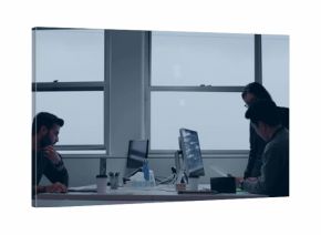 Collaborating professionals reviewing monitors and typing on laptop in office, with coffee cup