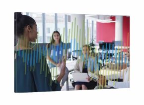 Presenting woman in green blouse gesturing at charts in office, with laptop wheelchair, copy space