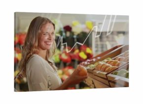 Smiling shopper in light blouse holding orange apple in produce aisle, graph overlay, copy space